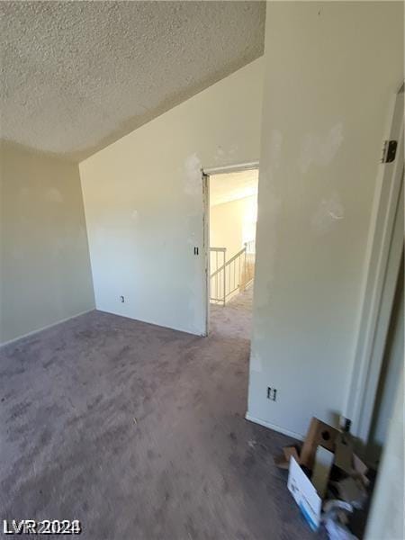 carpeted empty room with vaulted ceiling and a textured ceiling