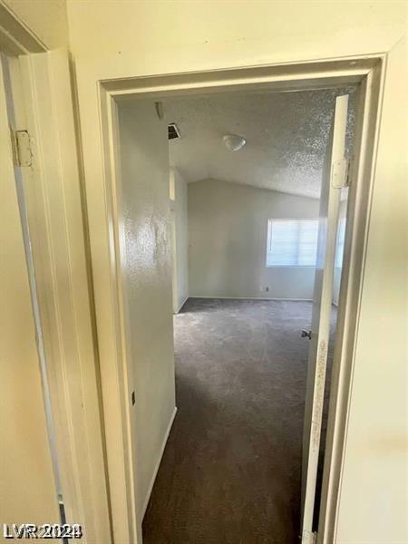 corridor with vaulted ceiling, a textured ceiling, and dark colored carpet