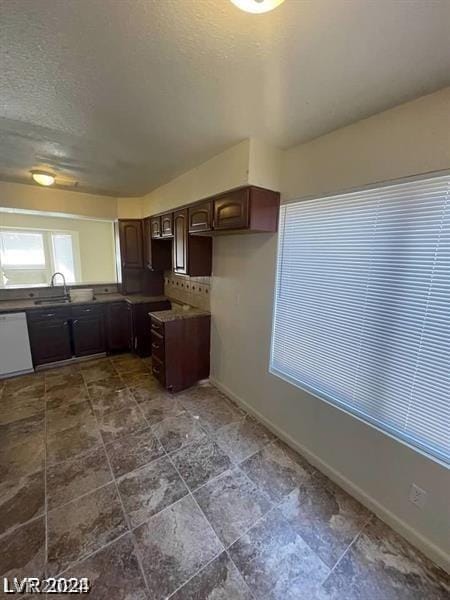 kitchen with sink, a textured ceiling, dark brown cabinets, white dishwasher, and backsplash