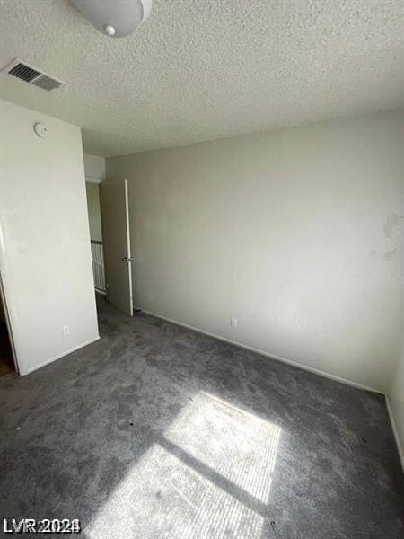 empty room with a textured ceiling and dark colored carpet