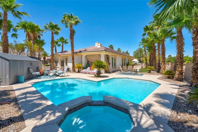 view of swimming pool with a storage shed, a patio area, and an in ground hot tub