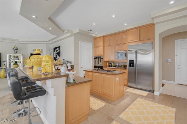 kitchen with built in appliances, light brown cabinetry, a kitchen bar, and a kitchen island