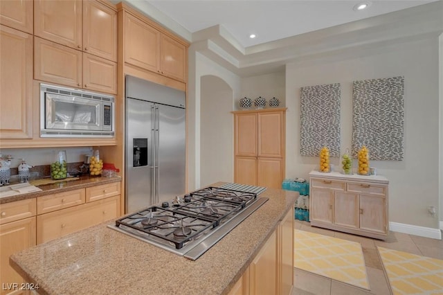 kitchen with built in appliances, light tile patterned floors, light stone countertops, and light brown cabinets