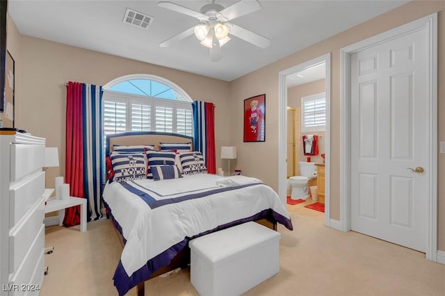 bedroom with multiple windows, ensuite bath, light colored carpet, and ceiling fan