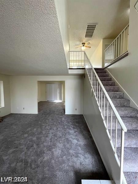 stairway with dark carpet, a textured ceiling, and ceiling fan