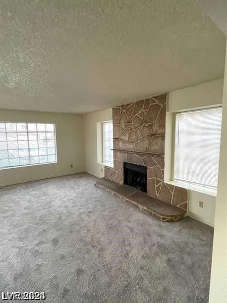 unfurnished living room featuring a textured ceiling, a fireplace, carpet, and a healthy amount of sunlight