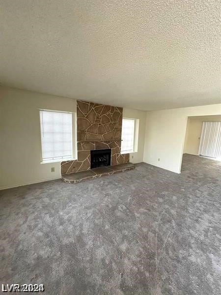 unfurnished living room with a stone fireplace, carpet floors, and a textured ceiling