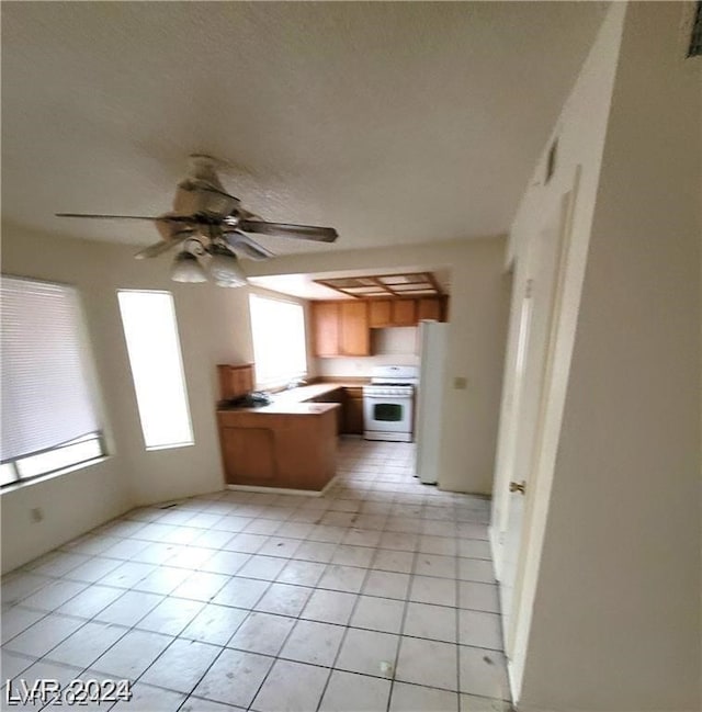 kitchen featuring white fridge, ceiling fan, kitchen peninsula, stove, and light tile patterned floors