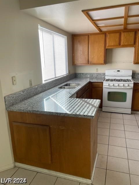 kitchen with light tile patterned flooring, gas range gas stove, sink, and kitchen peninsula