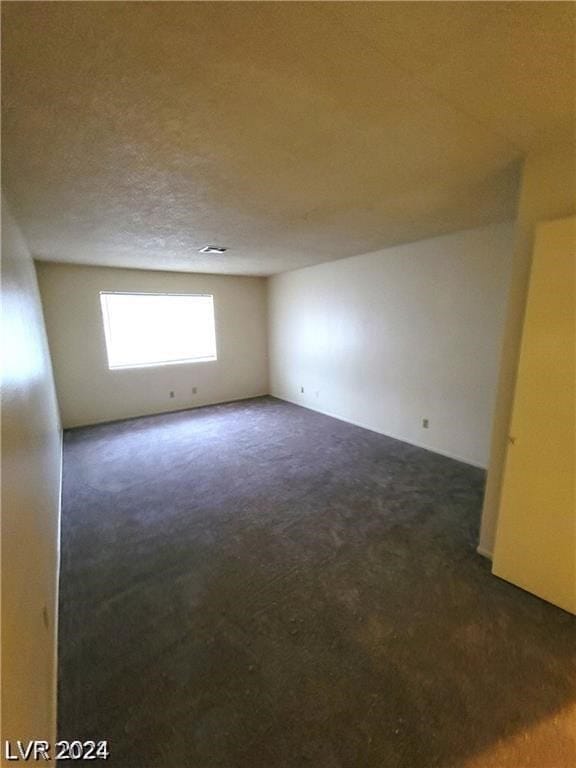 spare room featuring a textured ceiling and dark carpet