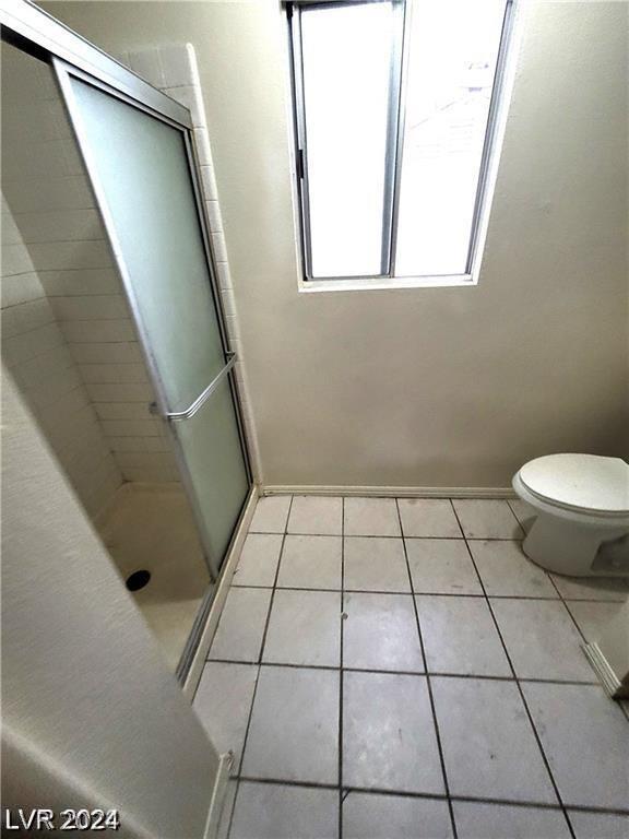 bathroom featuring tile patterned flooring, a shower with door, and toilet