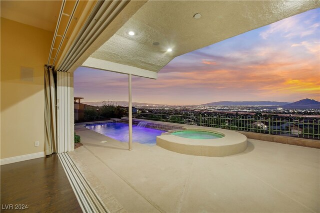 pool at dusk featuring a mountain view, pool water feature, an in ground hot tub, and a patio