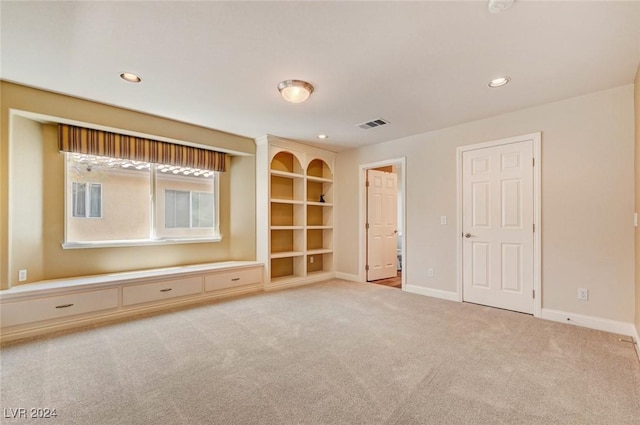 unfurnished living room featuring built in shelves and light colored carpet