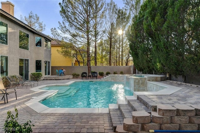 view of pool with a patio area, fence, and a pool with connected hot tub