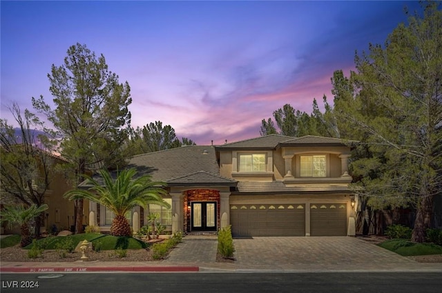 view of front of home with stucco siding, an attached garage, driveway, and french doors