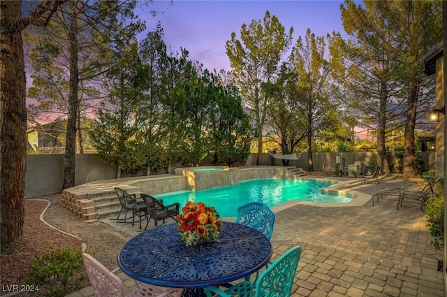 pool at dusk featuring a patio area and an in ground hot tub