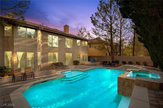 pool at dusk with a fenced in pool, fence, an in ground hot tub, and a patio area