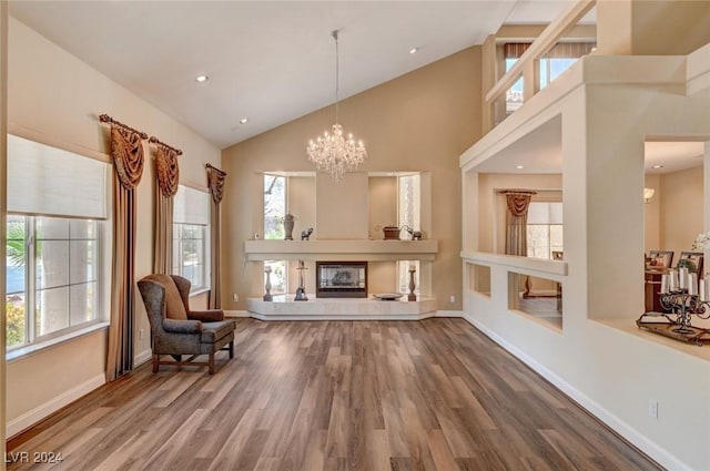 sitting room featuring a notable chandelier, high vaulted ceiling, a glass covered fireplace, wood finished floors, and baseboards