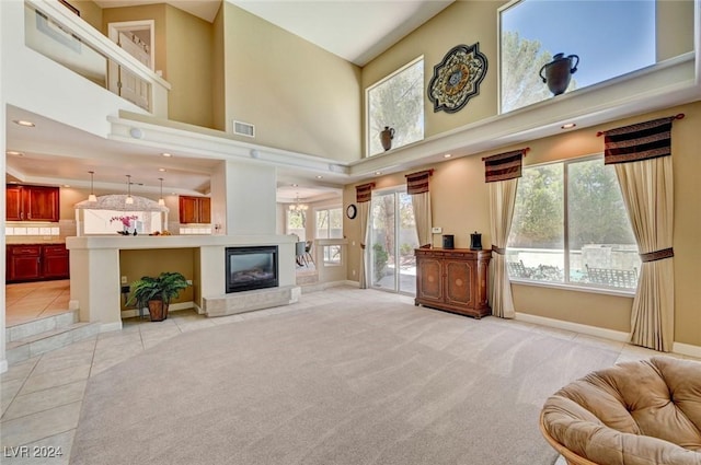 living room with a high ceiling, a tile fireplace, light colored carpet, and plenty of natural light