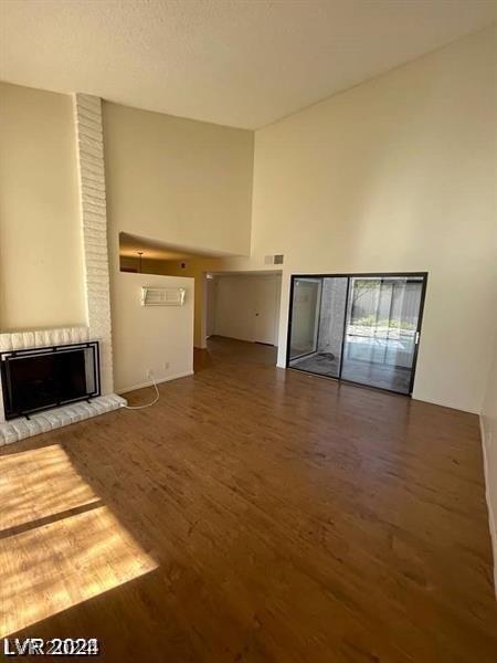 unfurnished living room featuring brick wall, a fireplace, wood-type flooring, and a high ceiling