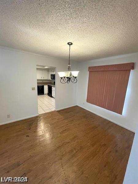 unfurnished dining area with an inviting chandelier, a textured ceiling, and light hardwood / wood-style flooring