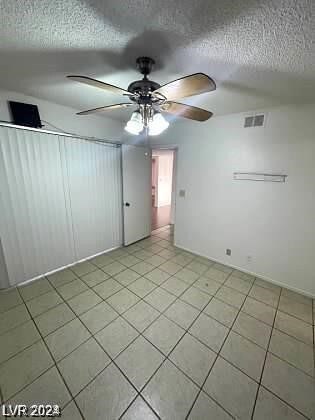 empty room featuring a textured ceiling, ceiling fan, and light tile patterned floors