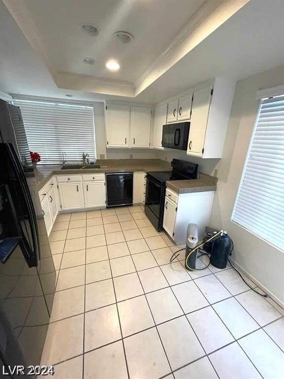 kitchen featuring light tile patterned flooring, black appliances, a tray ceiling, white cabinets, and sink