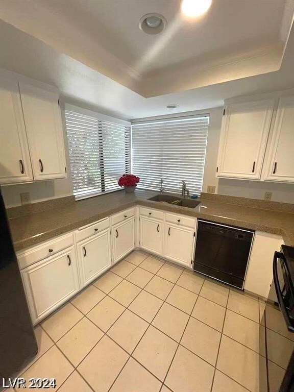 kitchen with black dishwasher, sink, light tile patterned floors, white cabinetry, and a raised ceiling