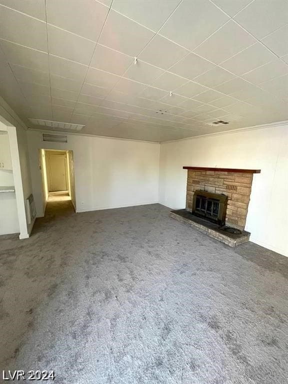 unfurnished living room with a stone fireplace, ornamental molding, and carpet flooring