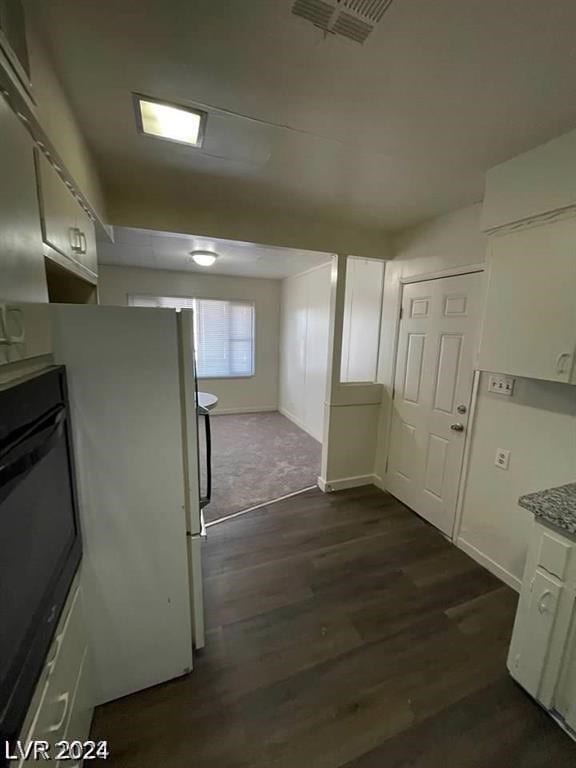 kitchen with dark wood-type flooring, white fridge, light stone counters, and white cabinets