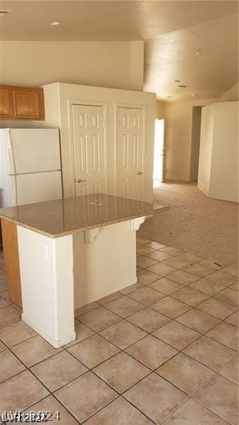 kitchen with light tile patterned flooring, a breakfast bar, stone countertops, white refrigerator, and a kitchen island