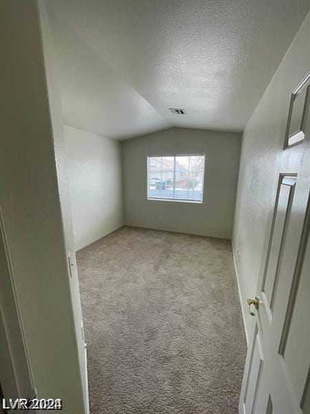 spare room featuring light colored carpet, lofted ceiling, and a textured ceiling