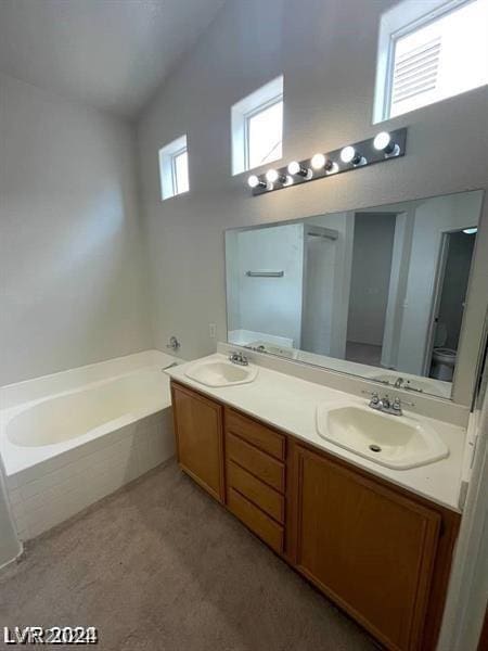 bathroom with tiled tub, vaulted ceiling, vanity, and toilet