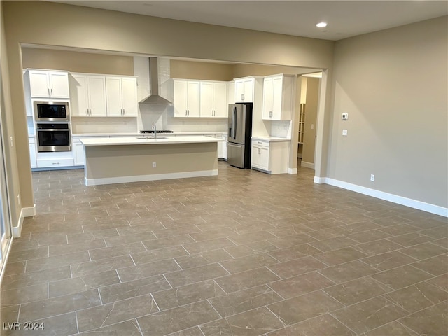 kitchen with white cabinets, appliances with stainless steel finishes, a kitchen island with sink, and wall chimney exhaust hood