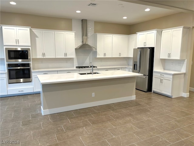 kitchen with a center island with sink, wall chimney range hood, decorative backsplash, appliances with stainless steel finishes, and white cabinetry