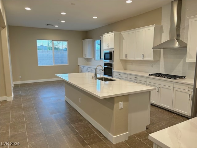 kitchen featuring white cabinets, stainless steel appliances, a kitchen island with sink, and wall chimney range hood