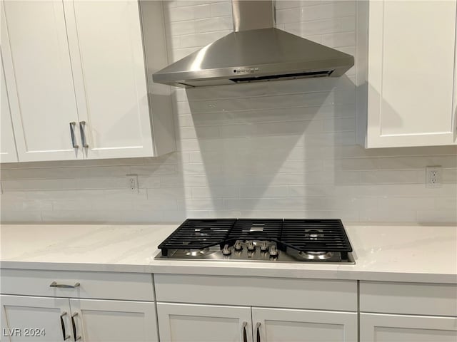 kitchen featuring white cabinetry, light stone counters, wall chimney range hood, and stainless steel gas cooktop