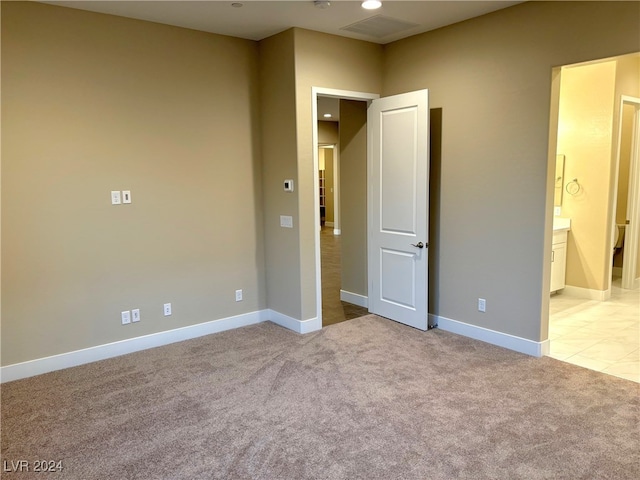 unfurnished bedroom featuring light carpet and ensuite bathroom