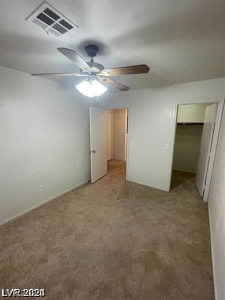 unfurnished bedroom featuring a spacious closet, light colored carpet, a closet, and ceiling fan