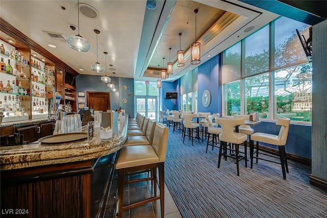 bar with decorative light fixtures, stone countertops, and a tray ceiling