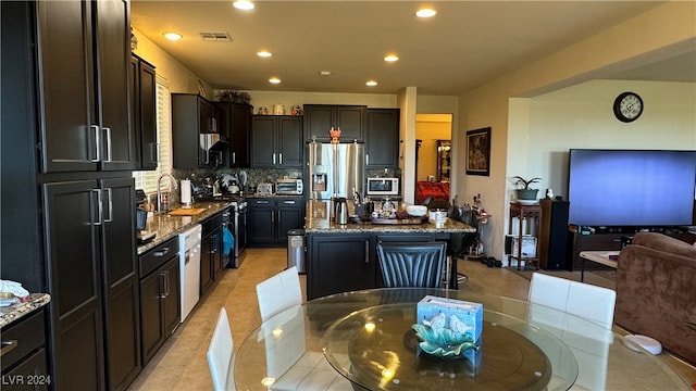 kitchen with stainless steel appliances, light tile patterned floors, a kitchen island, decorative backsplash, and light stone countertops