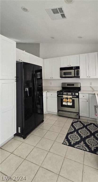 kitchen with white cabinets, stainless steel appliances, vaulted ceiling, and light tile patterned floors