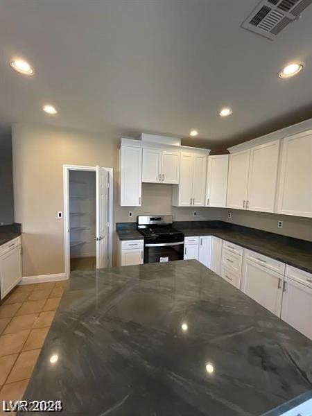 kitchen with white cabinets, light tile patterned flooring, dark stone counters, and stainless steel range with electric stovetop