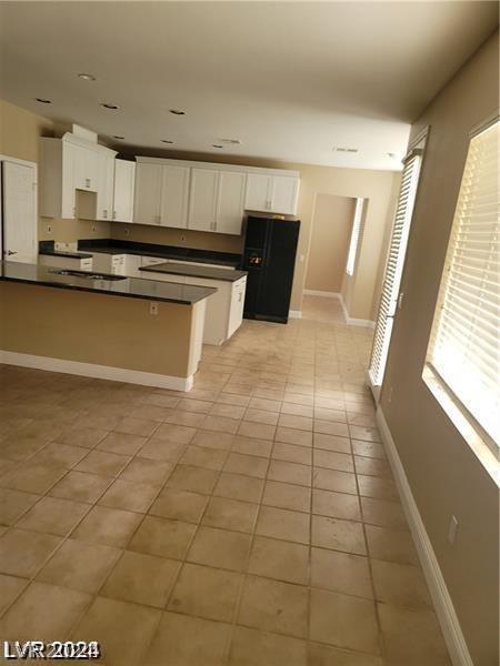 kitchen with white cabinetry, black refrigerator with ice dispenser, and light tile patterned floors