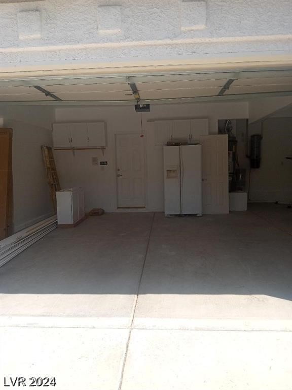 garage with a garage door opener and white refrigerator with ice dispenser