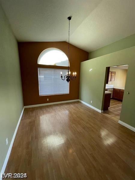 unfurnished dining area with baseboards, lofted ceiling, an inviting chandelier, and wood finished floors