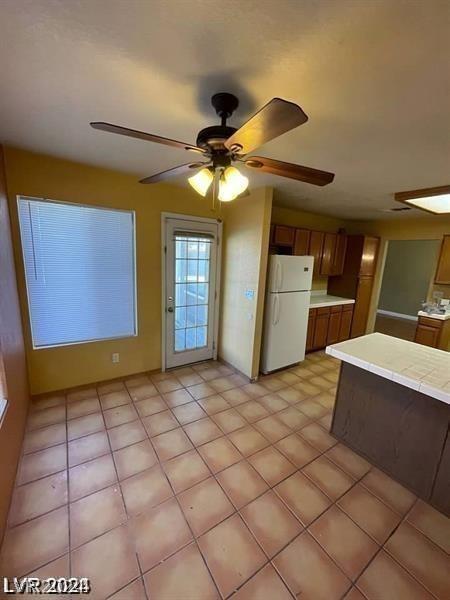 kitchen featuring brown cabinets, a ceiling fan, and freestanding refrigerator