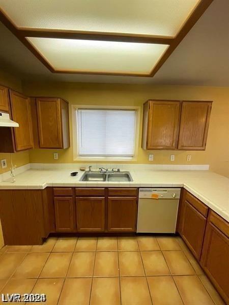 kitchen with dishwasher, brown cabinetry, under cabinet range hood, and a sink