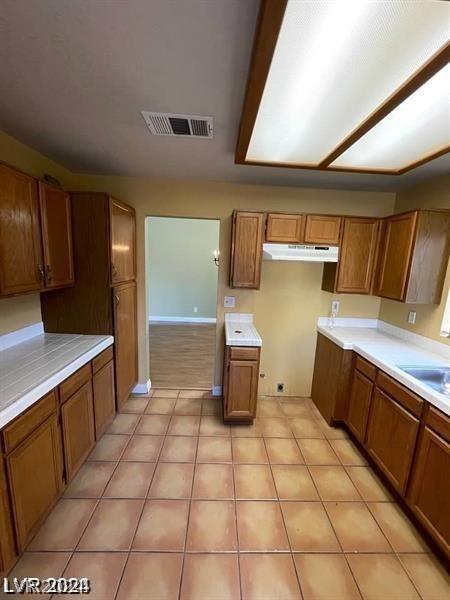 kitchen with brown cabinetry, visible vents, light countertops, and under cabinet range hood