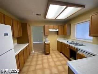 kitchen featuring visible vents, under cabinet range hood, freestanding refrigerator, brown cabinetry, and light countertops